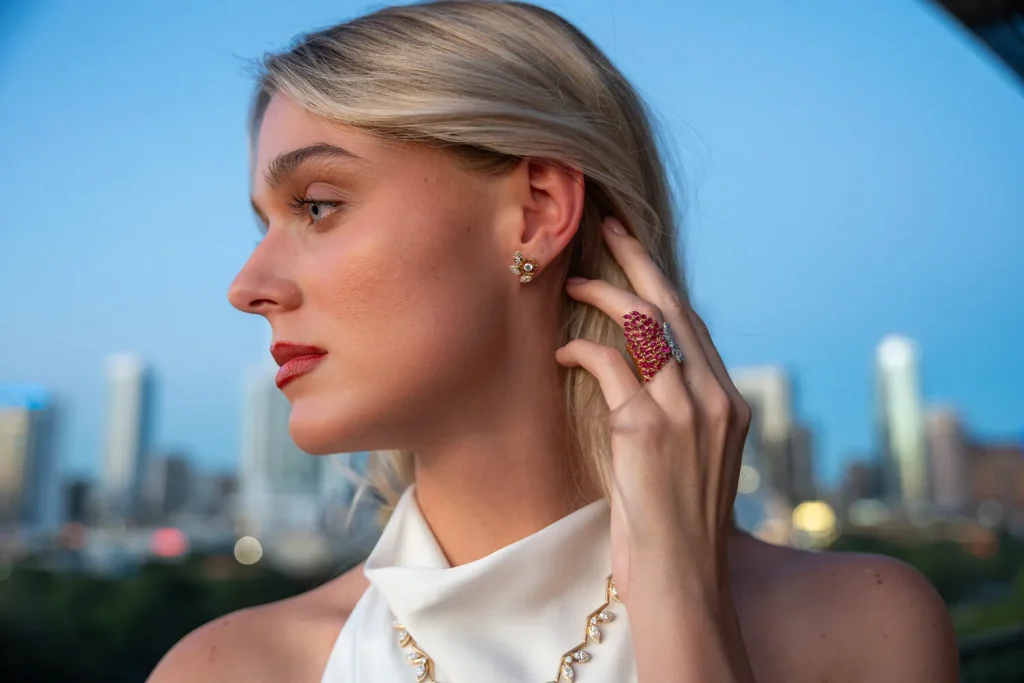 Model wearing diamond earrings and a ruby cocktail ring with the Austin skyline behind her, Eterna Jewels