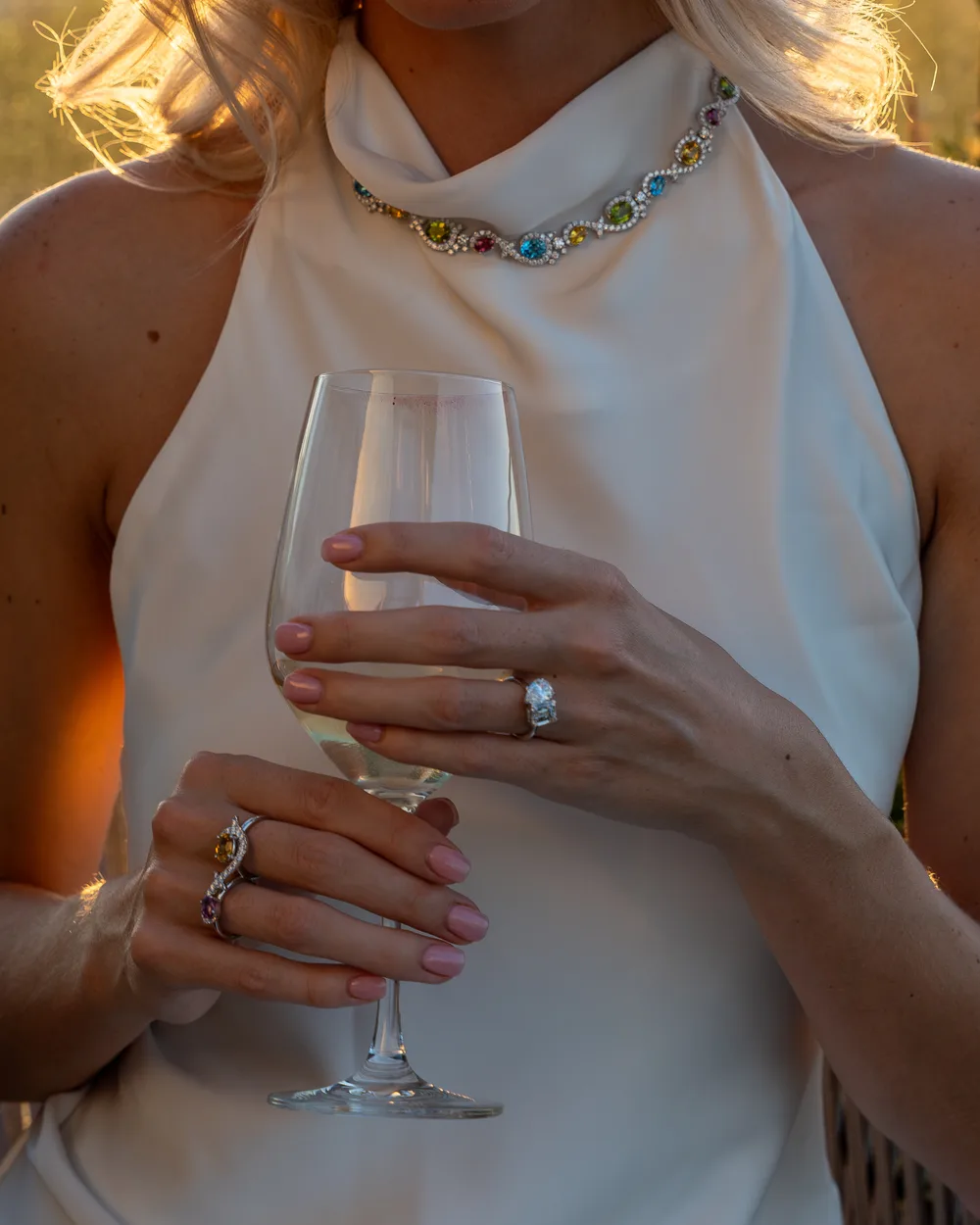Hands holding a wine glass, wearing a diamond ring and a gemstone ring